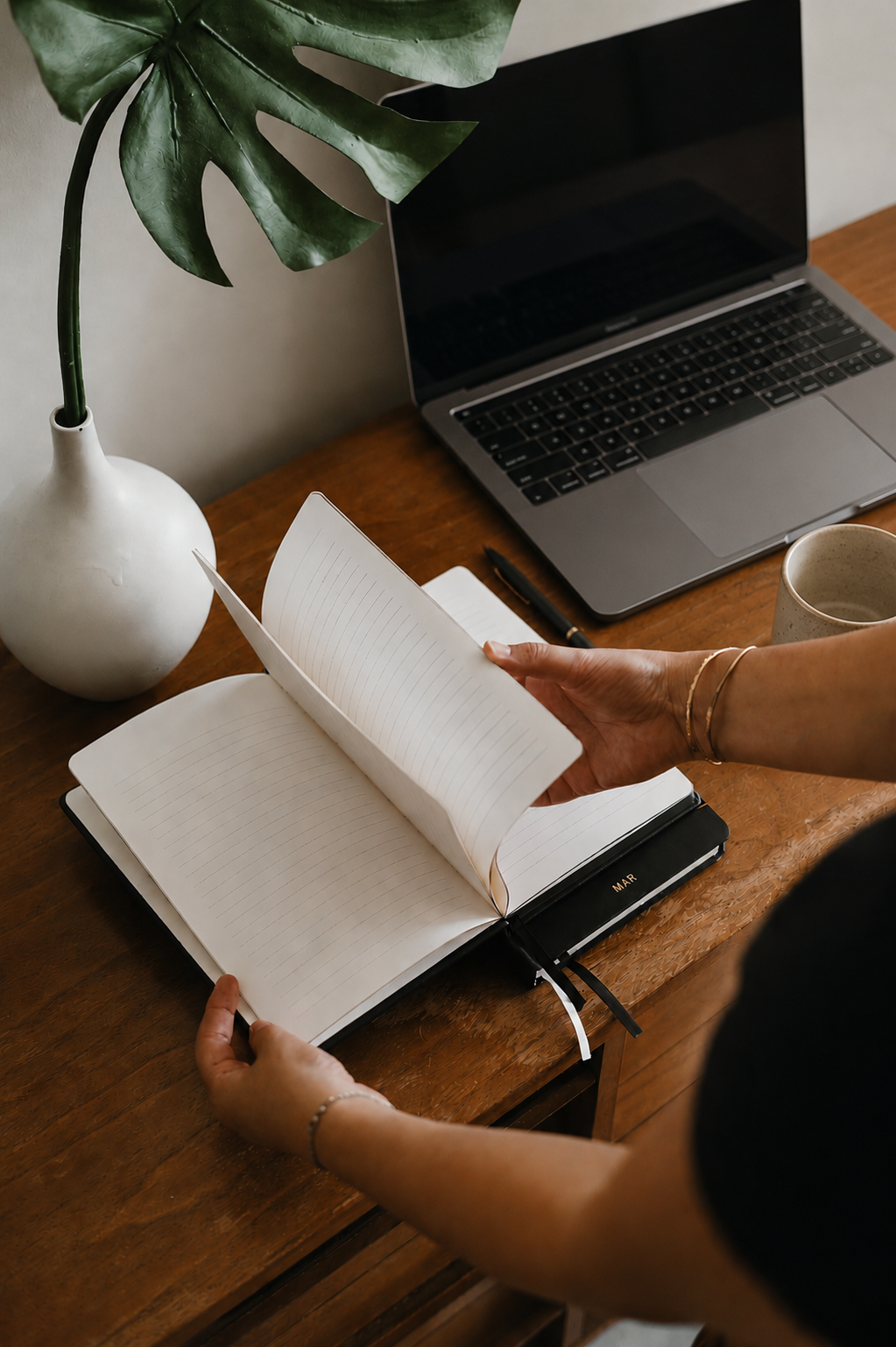 Hands paging through a planning notebook at a warm wooden desk